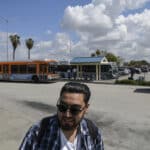 Alameda Post - Henry Sanchez, 22, who lives in Bell Gardens, waits for the Metro bus to arrive at the Norwalk Green Line Station in Norwalk on April 3, 2023. Pablo Unzueta for CalMatters