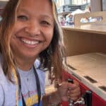 Alameda Post - A woman smiles at the camera and pours a drink at a festival.