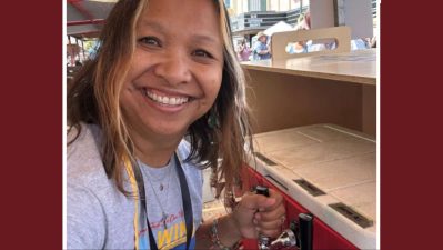 Alameda Post - A woman smiles at the camera and pours a drink at a festival.
