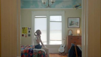 Alameda Post - A girl who appears to be in her teens sits on the bed of a childhood bedroom and talks on the phone.
