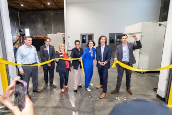 Alameda Post - a group of elected officials and Anthro Energy representatives smile and cut a ribbon in a warehouse