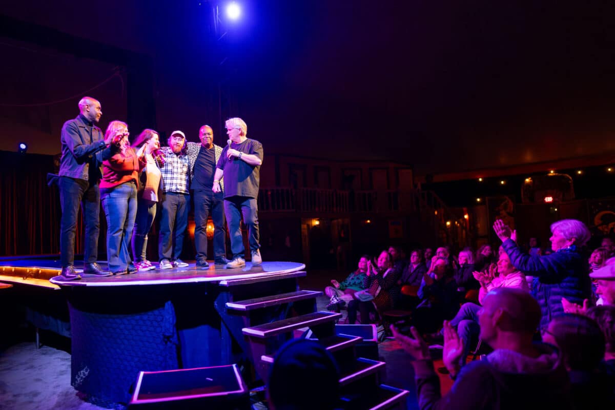 Alameda Post - Six performers stand together onstage and smile while the audience claps.
