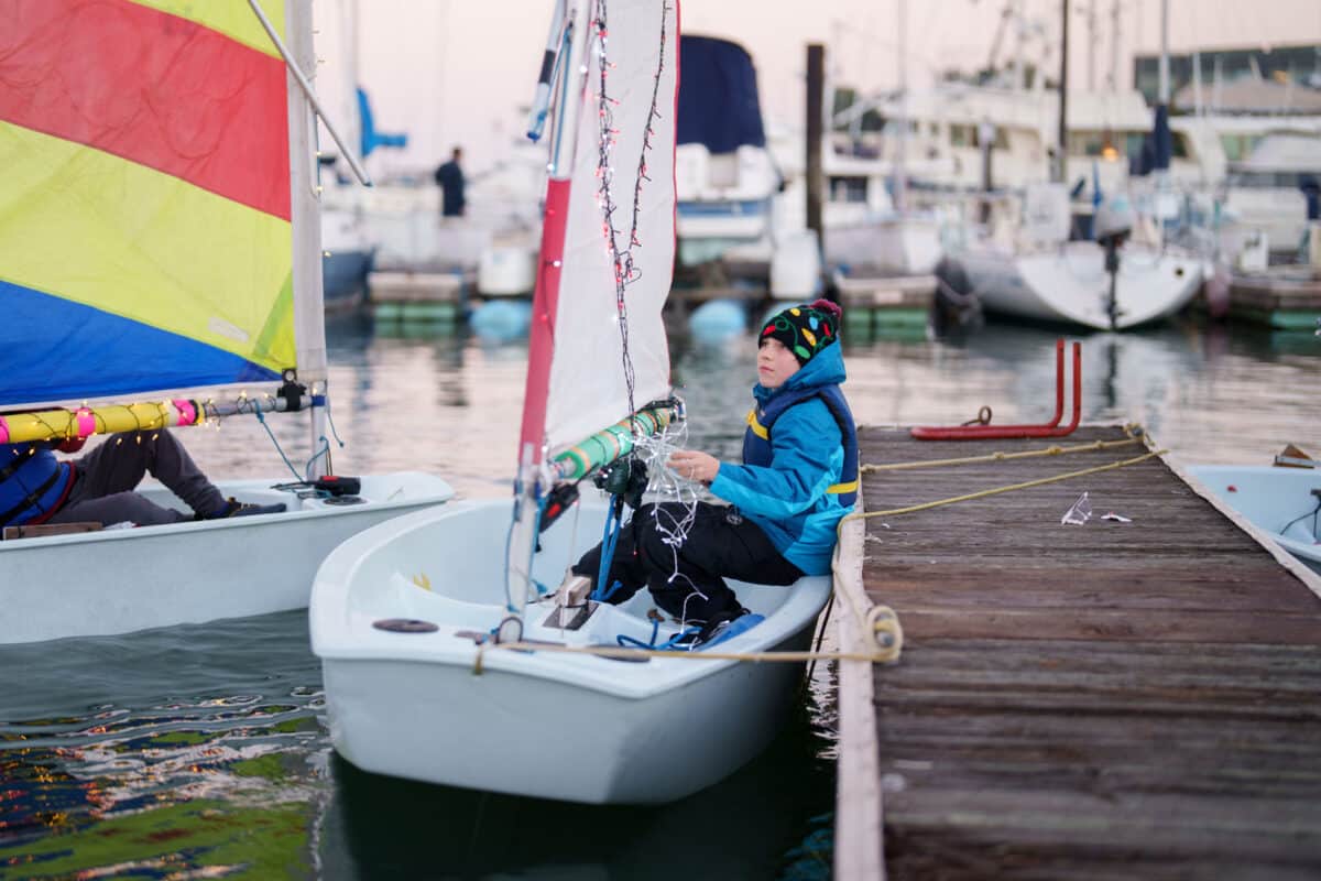 Alameda Post - A young sailor strings lights on a small sail boat.