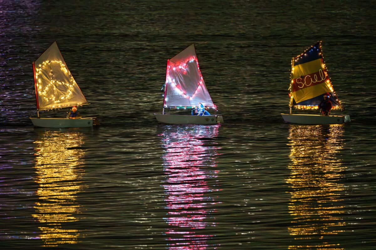 Alameda Post - Three young sailors in small boats ride by after sunset along the Estuary in lighted decorations. 
