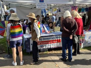 Alameda Post - a booth with a petition for Ranked Choice Voting. People walk around wearing rainbow attire.