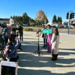 Alameda Post - camera crews look on as Mayor Ashcraft holds up a street sign which says Wilma Chan Way. Wilma's children stand next to the mayor.