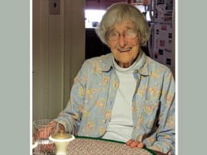 Alameda Post - Sally Faulhaber sits at a kitchen table and smiles.