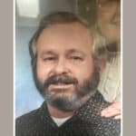Alameda Post - James Gary Stutler smiles in a photograph. A woman that appears to be close to his age stands behind him and smiles.