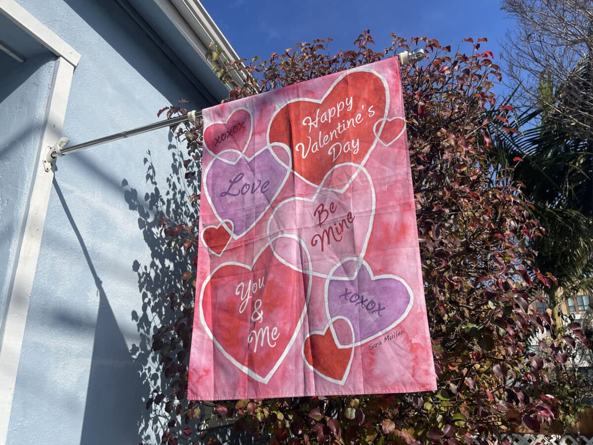 Alameda Post - A Valentine's Day flag hung outside a home. It depicts candy sweet hearts with phrases like "Love" and "Be Mine."