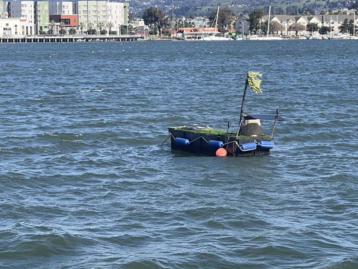 Alameda Post - A small floating platform out in the water with a fake tree, solar panel, and turf grass. It's a peculiar tiny manmade island. 