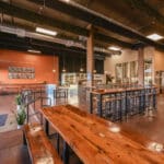 Alameda Post - the inside of Alameda Brewing's taproom. Lots of shining wooden tables and metal accepts decorate the open and well-let space