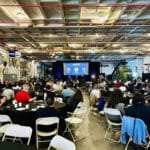 Alameda Post - tables fill a large room in the USS Hornet, and people gather to hear speakers at the Economic Forecast