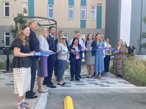 Alameda Post - Thirteen people smile and hold a ribbon in front of Linnet Corner and Estuary I. One of them cuts the ribbon.