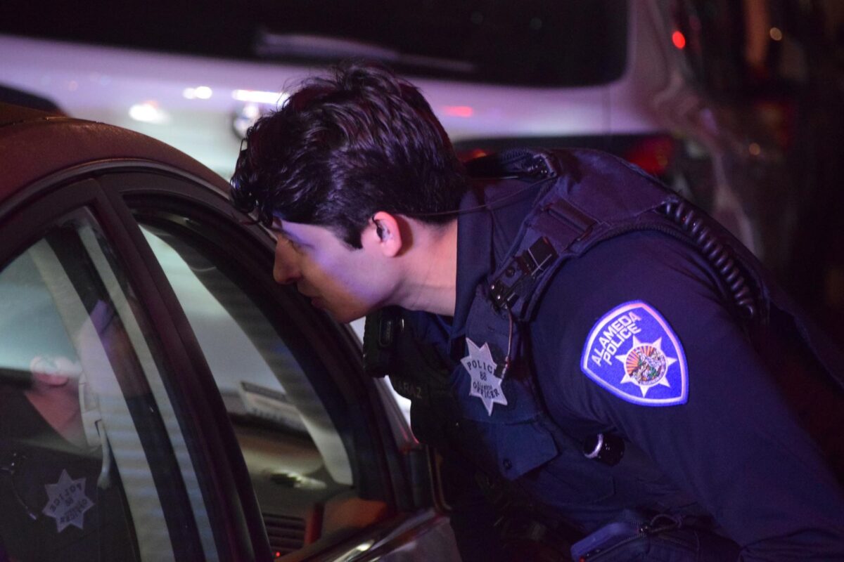 Alameda Post - An APD officer leans over to speak to somebody out of frame in a car.
