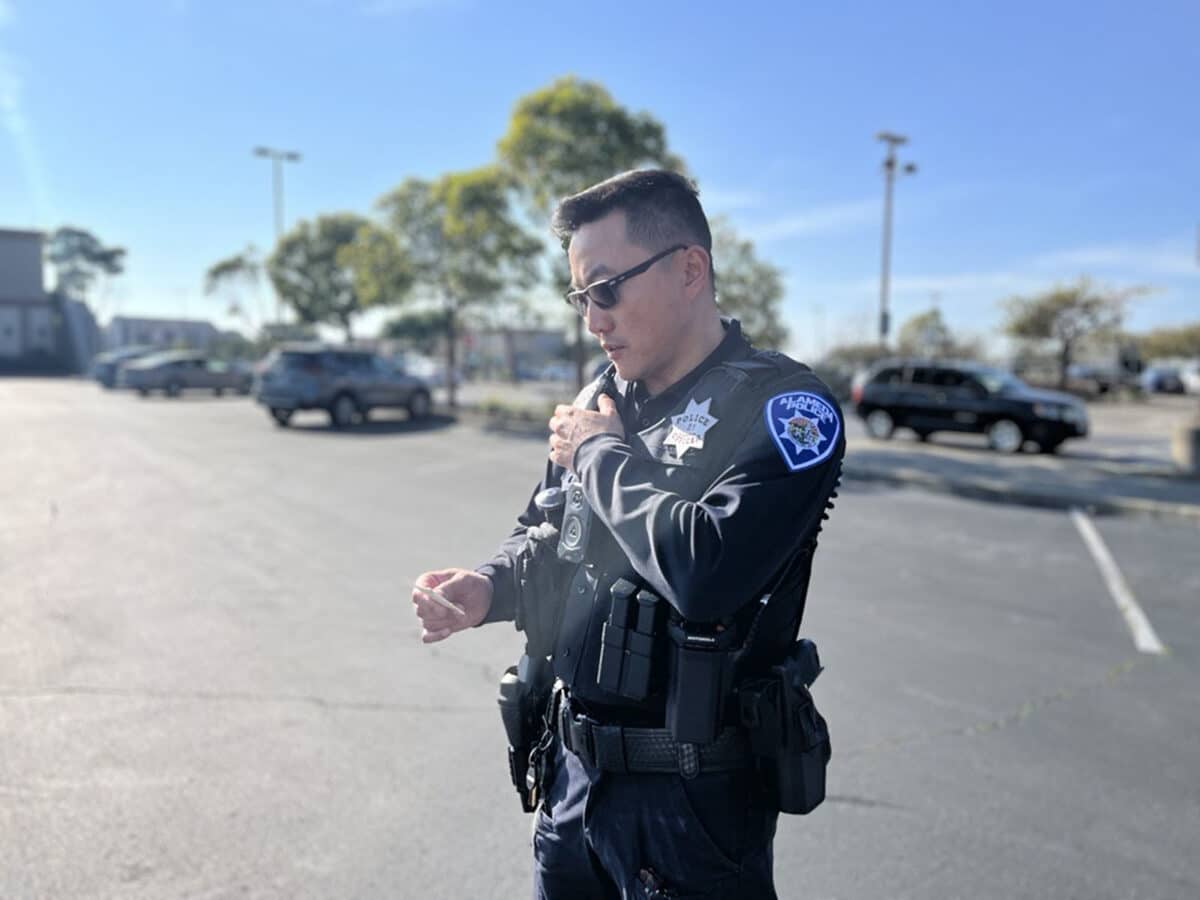 Alameda Post - An APD officer speaks into a communication device on their shoulder.