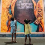 Alameda Post - two children look up at a mural of a woman wearing a shirt with the words "I am my ancestors' wildest dreams."