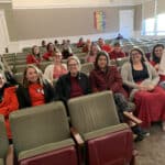 Alameda Post - AUSD teachers wearing red sit in the audience of a board meeting. One teacher holds a sign that says, "I support my students. I should be able to support my family."