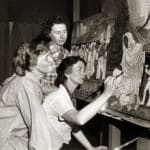 Alameda Post - a black and white photo of the Bruton sisters gathered around a painting while one lifts a paint brush
