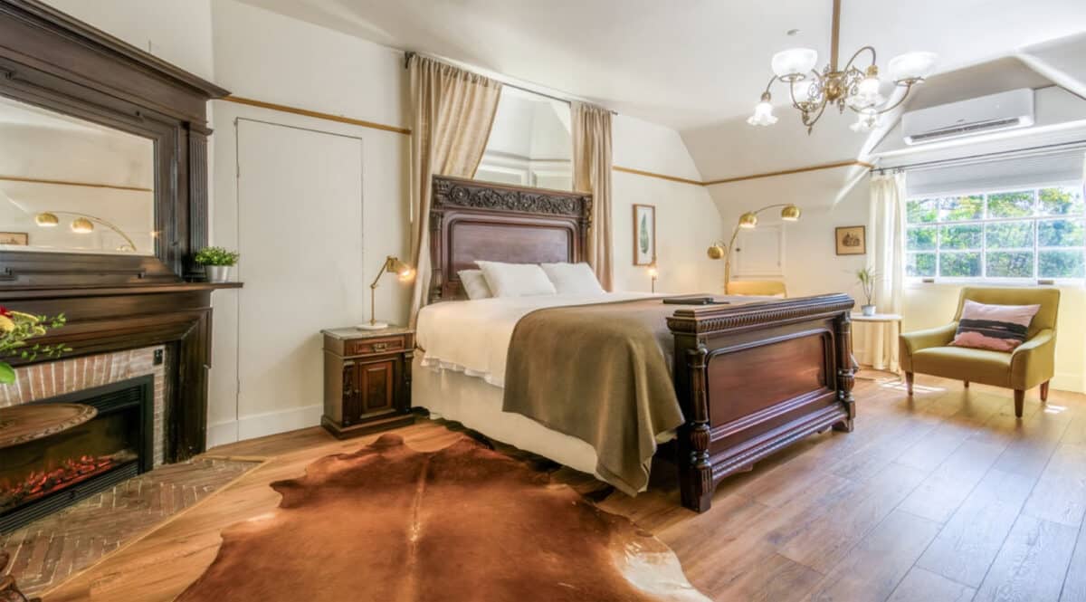 Alameda Post - A large, brightly lit hotel room with a fireplace and grand wooden bed frame. 