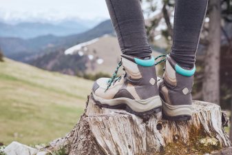 Alameda Post - A person wearing hiking boots stands on a stump and looks out at the scenery. Only their calves and feet are visible.
