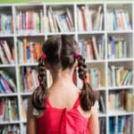 Alameda Post - A young girl stands and looks at a wall of books in a library.