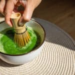 Alameda Post - A hand using a bamboo whisk to froth vibrant green matcha tea