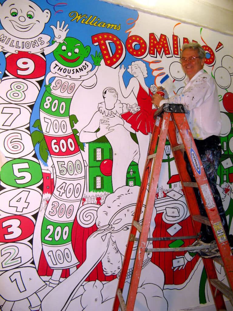 Alameda Post - Ed Cassel stands on top of a ladder and smiles while painting a mural