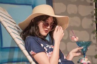 Alameda Post - Emilia Arneson onstage in a wide beach hat, with a tropical looking glass, on a beach chaid