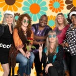 Alameda Post - A group photo of six woman in 60x style clothing in front of a flower background.