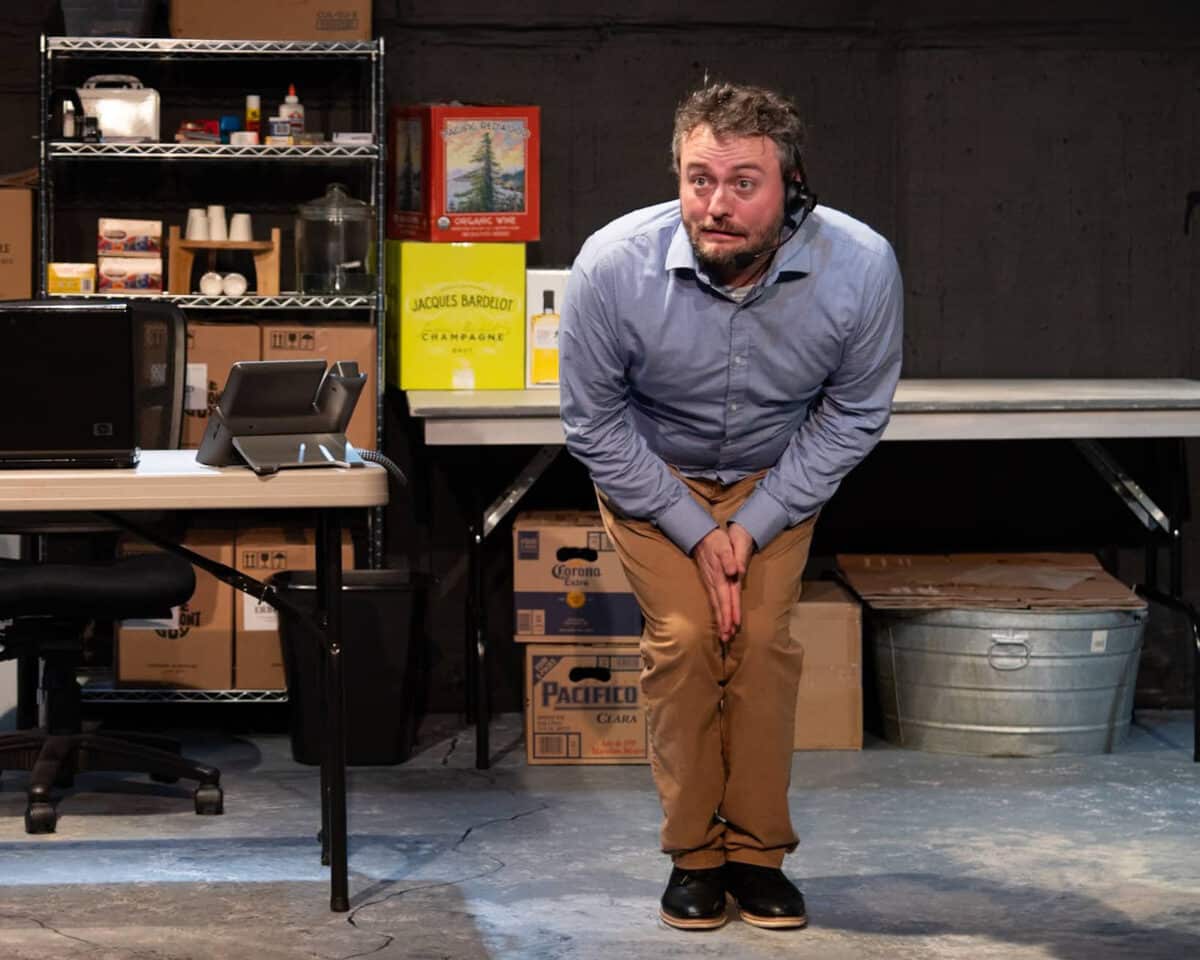 Alameda Post - An actor in a button up shirt and khakis is standing onstage. He is bent over with his hands in between his legs, looking nervous or wound up. 