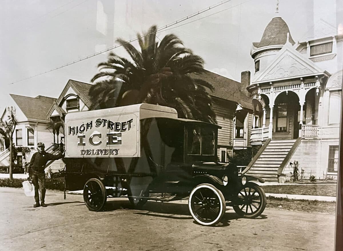 Alameda Post - a black and white photo of a very old car in front of a grand house. The side of the vehicle says "High Street Ice Delivery," and a man stands beside the truck with a large block of ice.