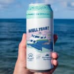 Alameda Post - A hand holds a can of Hull Yeah! beer in front of the ocean.