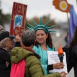 Alameda Post - A gathering of protestors, including a woman in a Statue of Liberty outfit and someone with a "Melt Ice" sign.