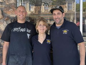 Alameda Post - two men and a woman stand in front of Domenico's Italian Deli wearing branded shirts