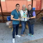 Alameda Post - Three people wearing Alameda Rum Stroll lanyards stand and smile with themed guides and shot glasses.