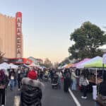 Alameda Post - Holiday shoppers view booths at the Winter Market in front of the theater's neon sign.