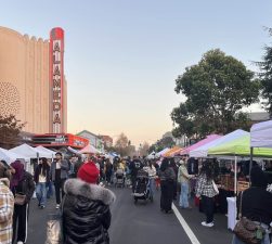 Alameda Post - Holiday shoppers view booths at the Winter Market in front of the theater's neon sign.