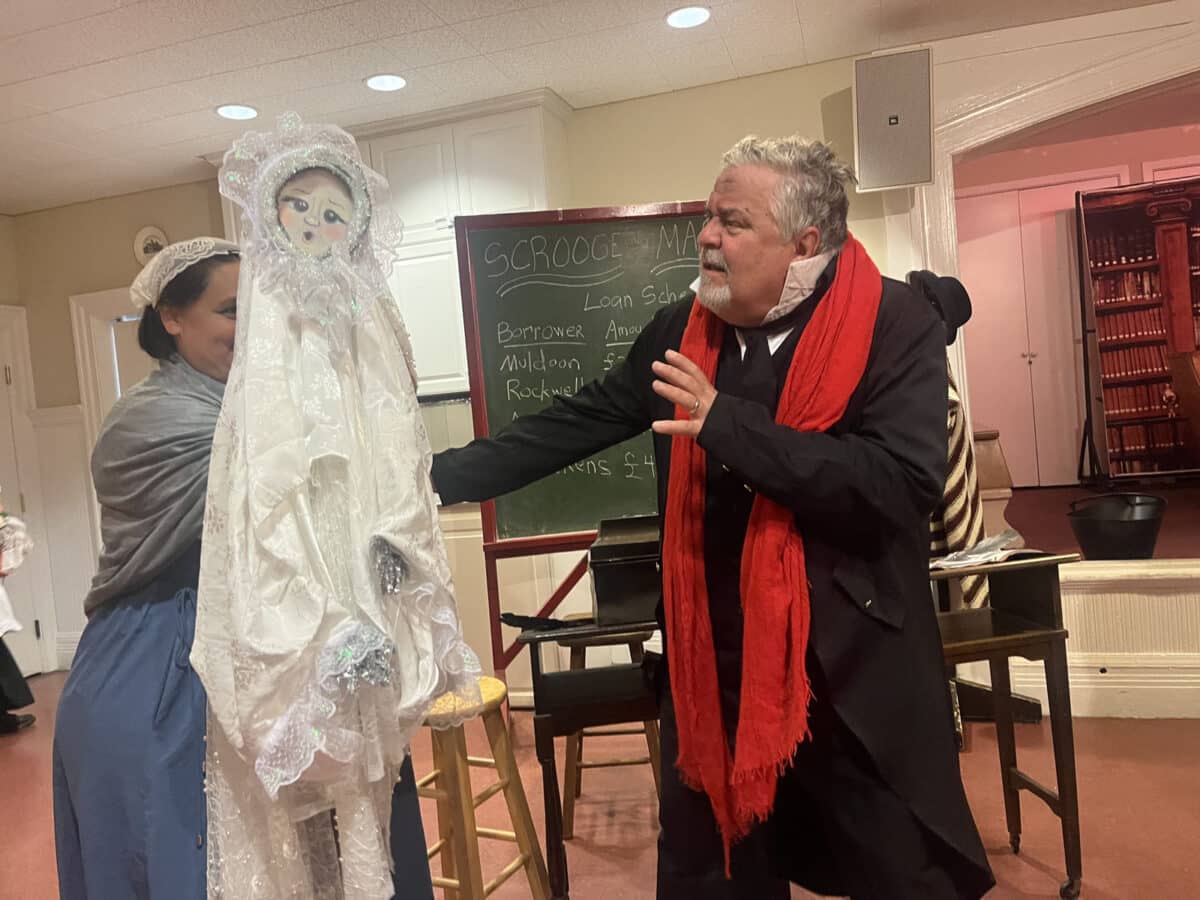 Alameda Post - On a simple set for The Christmas Carol, an actor talks with a doll representing a ghost.
