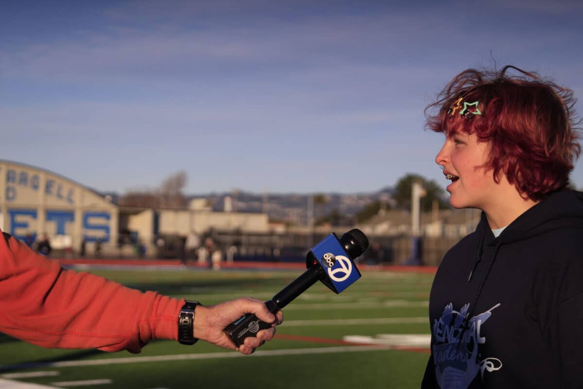Alameda Post - a student speaks into a microphone held by a news person. 
