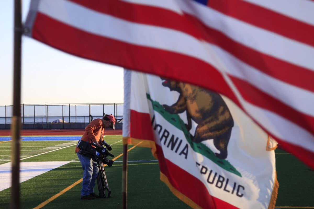 Alameda Post - A camera operator on the new Encinal field, with the American and California flags waving in the foreground. 