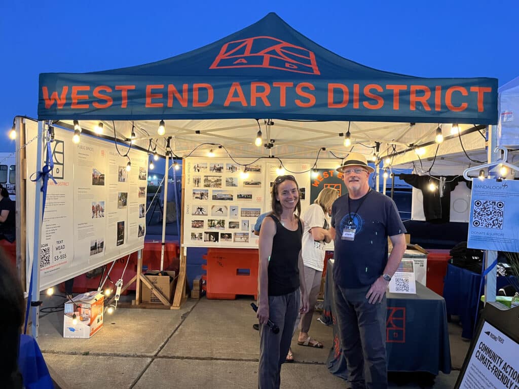 Alameda Post - at a tent or booth, two people stand and smile at the camera