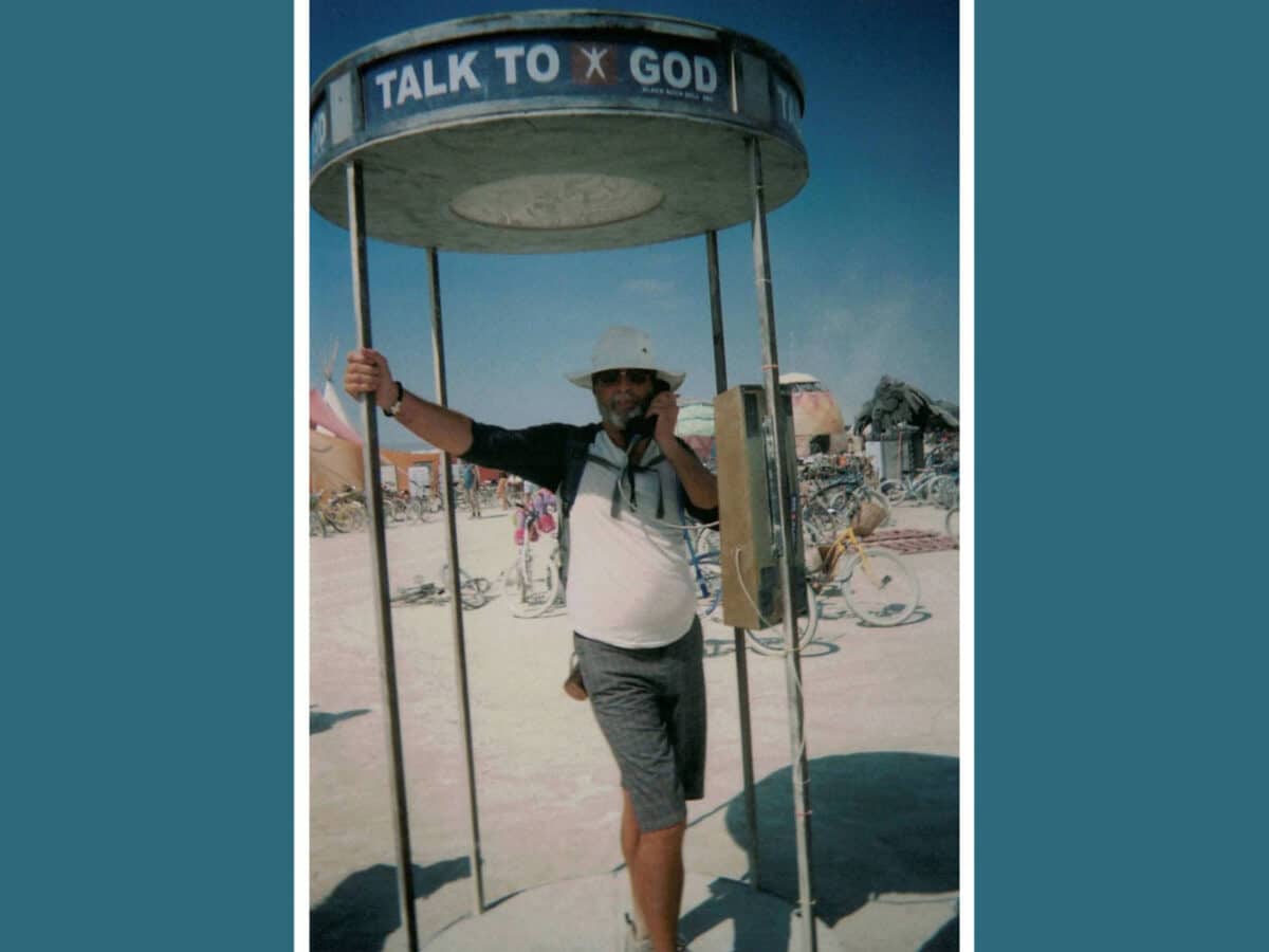 Alameda Post - a photo of Joseph Bryan "Joe" Devine. He is standing in a type telephone booth, which says "Talk to God."