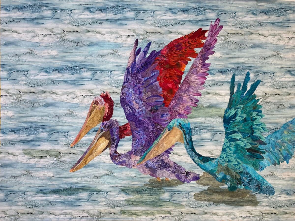 Alameda Post - A colorful quilt of three pelicans landing in the water.