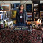Alameda Post - Lisa Haderlie Baker stands at a table surrounded by art