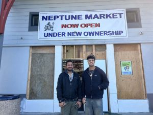 Alameda Post - The new owners of Neptune Market stand in front of the store's doors and smile.