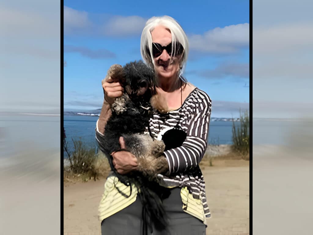 Alameda Post - Patricia Edith holds a small dog and waves its paw at the camera