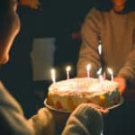 Alameda Post - one person hands a birthday cake with candles to another