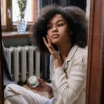 Alameda Post - a woman sits in front of a mirror and rubs a cream into her skin