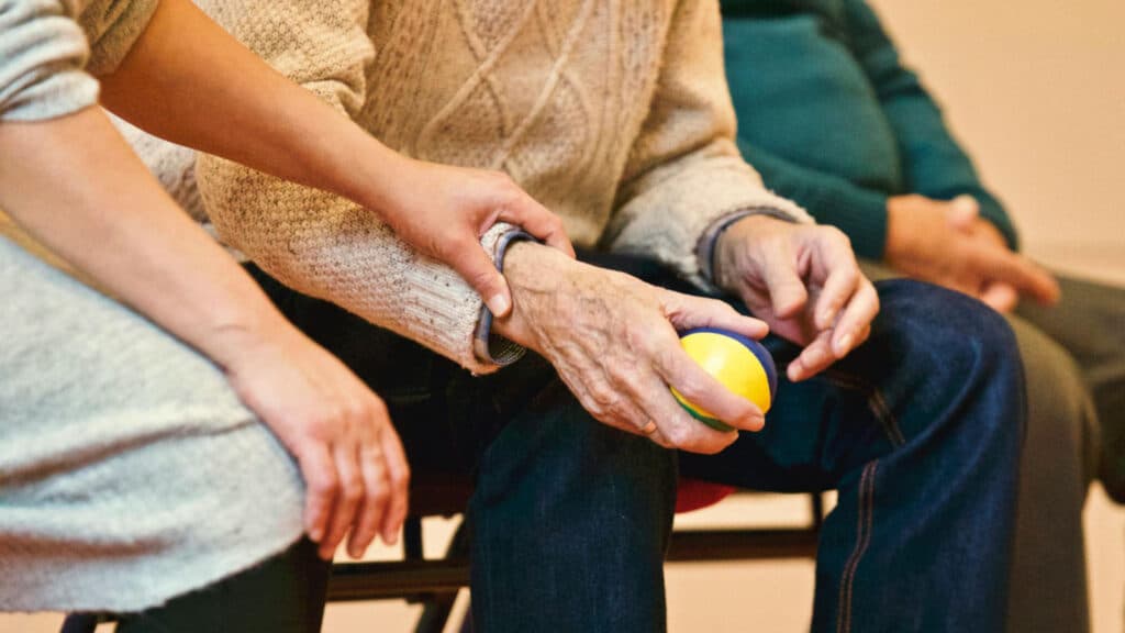 Alameda Post - an older adult holds a physical therapy ball in their hand, while a younger person places their hand over the older person's arm