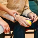 Alameda Post - an older adult holds a physical therapy ball in their hand, while a younger person places their hand over the older person's arm